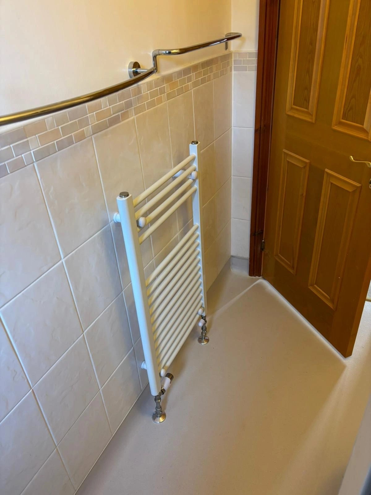 Tiled bathroom with a chrome ladder towel rail fixed to the wall